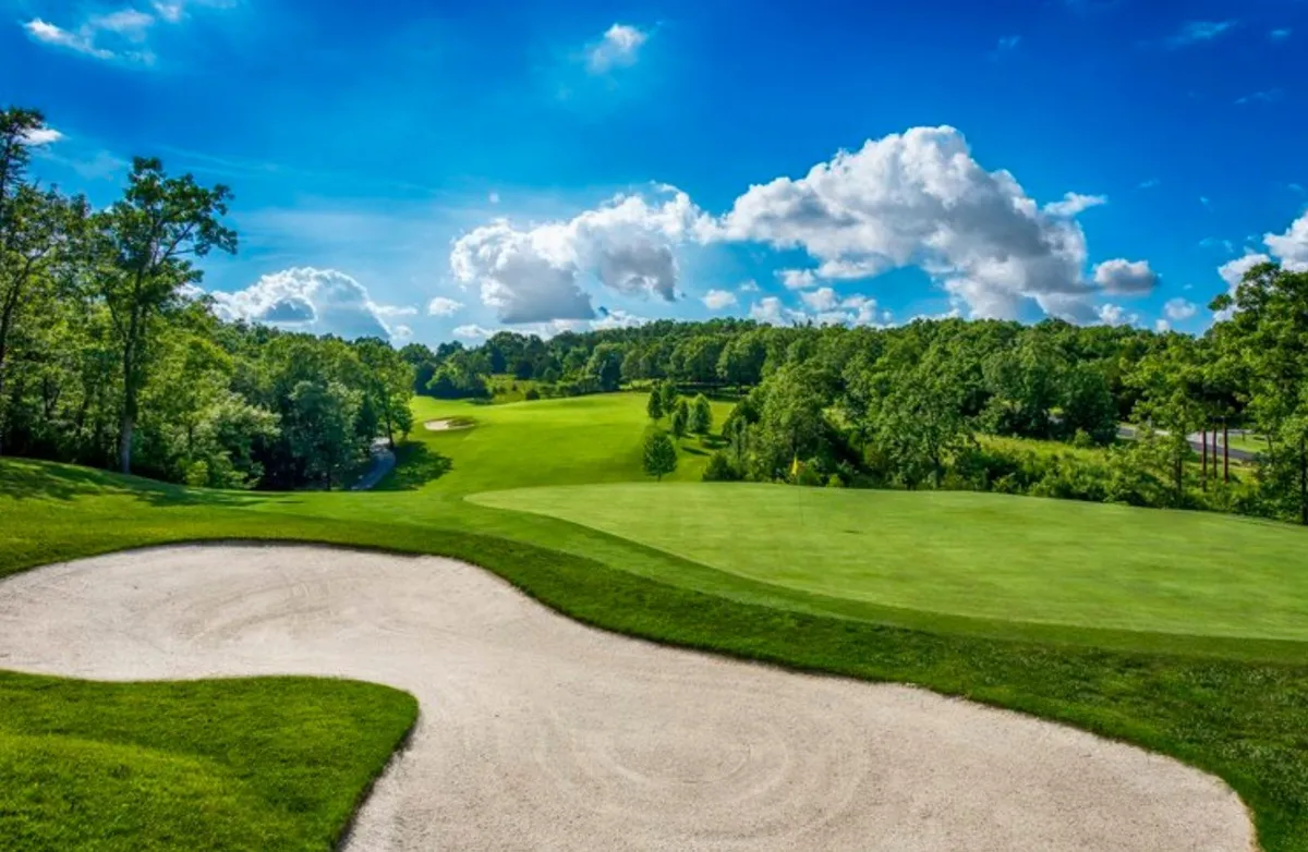 This image captures a scenic view of the Ledgestone Golf Course, featuring a well-manicured green, a sand trap, lush greenery, and an open blue sky. The tranquil setting invites viewers to imagine themselves teeing off or simply relaxing on the course.