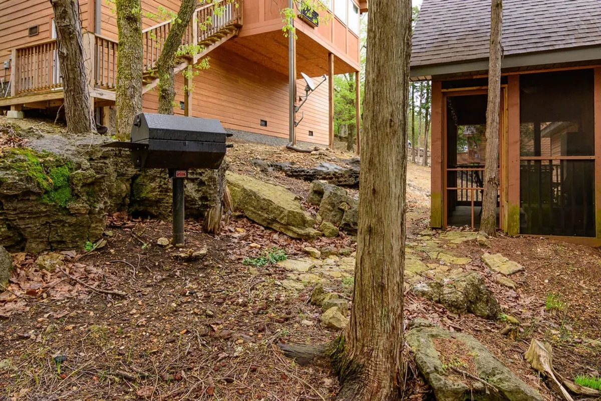 An exterior shot showing a wooden deck with a visible screened porch area, along with a barbecue grill and a scenic, rocky natural landscape. The image blends the sheltered comfort of the screened porch with open-air amenities and beautiful surroundings.