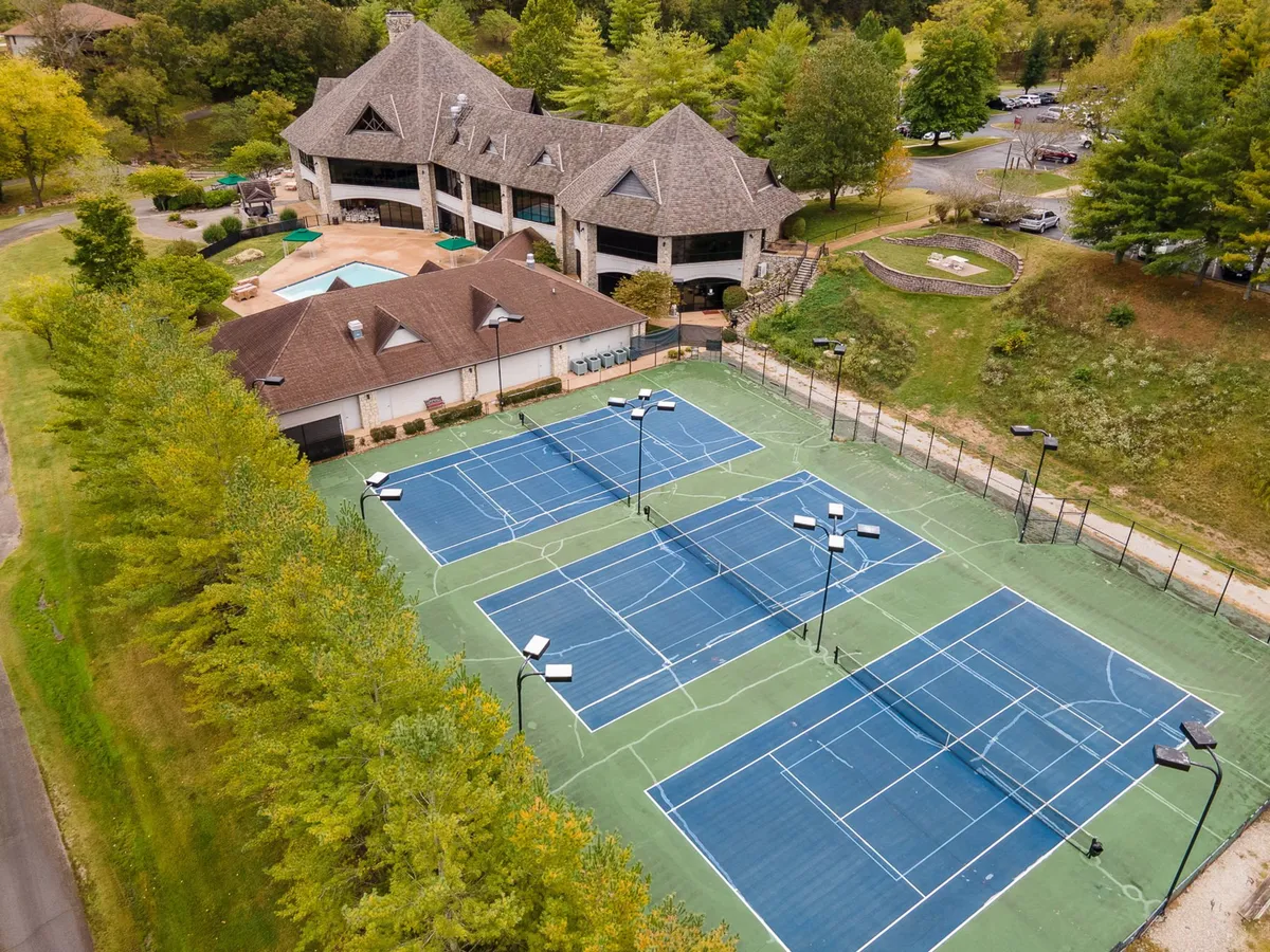 The tennis courts and clubhouse are shown amid lush greenery, highlighting recreational opportunities within the community. The clubhouse’s inviting design hints at social gatherings and after-activity relaxation.