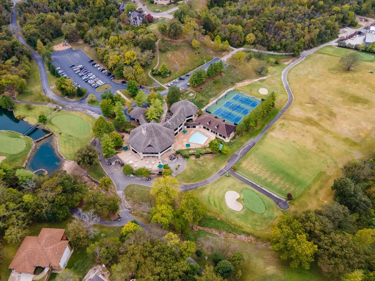 A lively resort exterior featuring an outdoor pool, tennis courts, golf course, and a serene pond, all adjacent to the main resort building. The scene is bustling with opportunities for swimming, tennis, golfing, and relaxing in the sun, embodying a resort atmosphere with diverse activities.